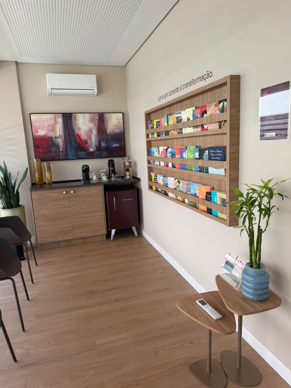 Canto da sala de espera com cafeteira, plantas e a parede de livros